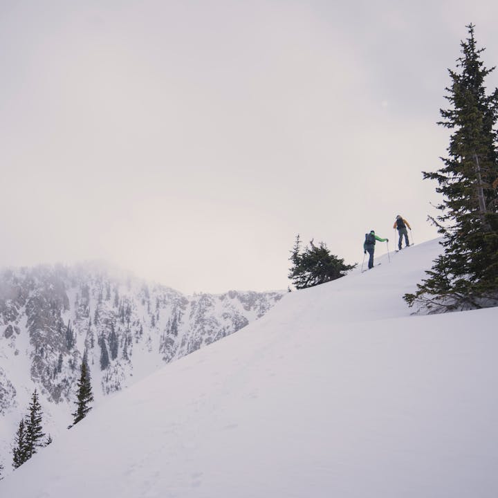 Two ski tourers work their way up a ridge with steep lines on a ridge behind them. 