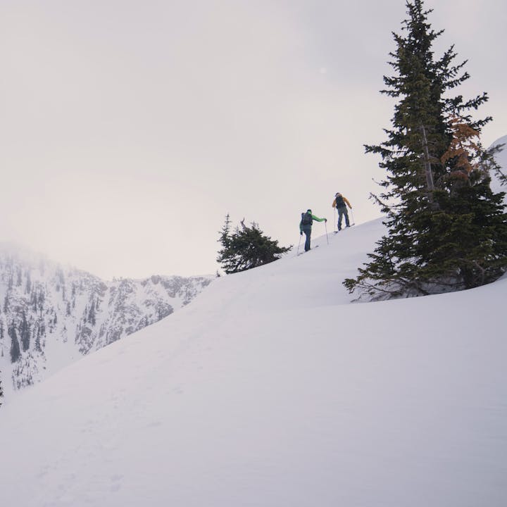 Two ski tourers work their way up a ridge with steep lines on a ridge behind them. 
