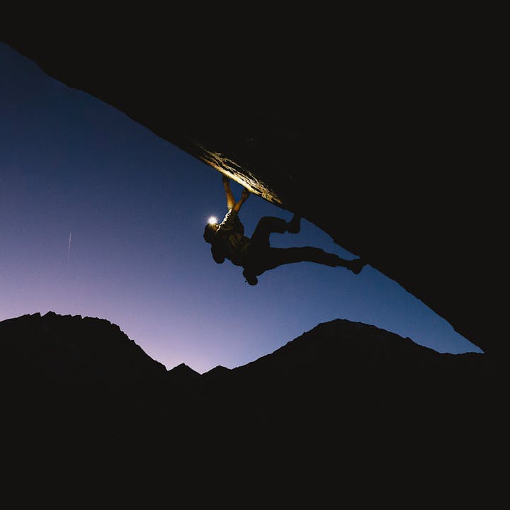 A boulderer on a problem in the dark, illuminating the way with a BD headlamp.