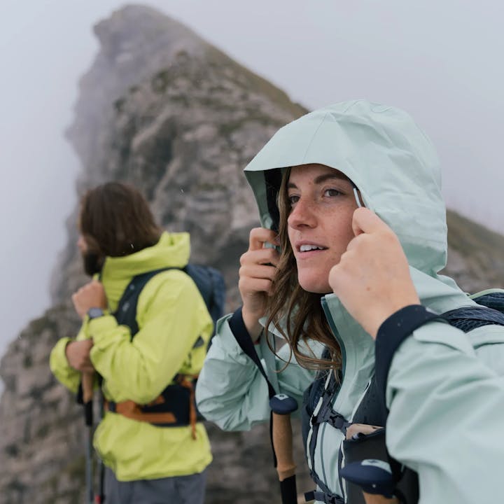 A hikers pulls up the hood on her rain jacket. 