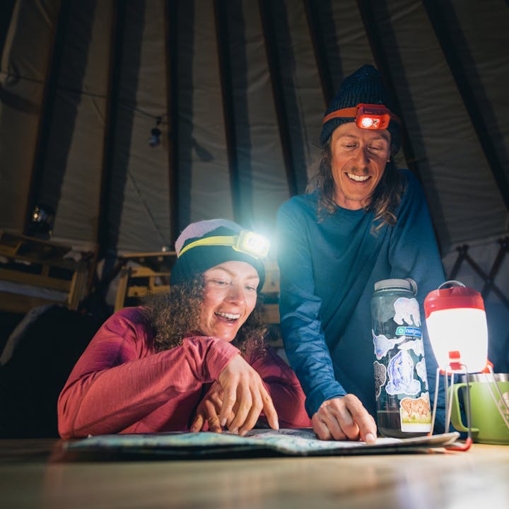 A pair of ski tourers plan a route in a yurt illuminated by a Black Diamond Apollo Lantern. 