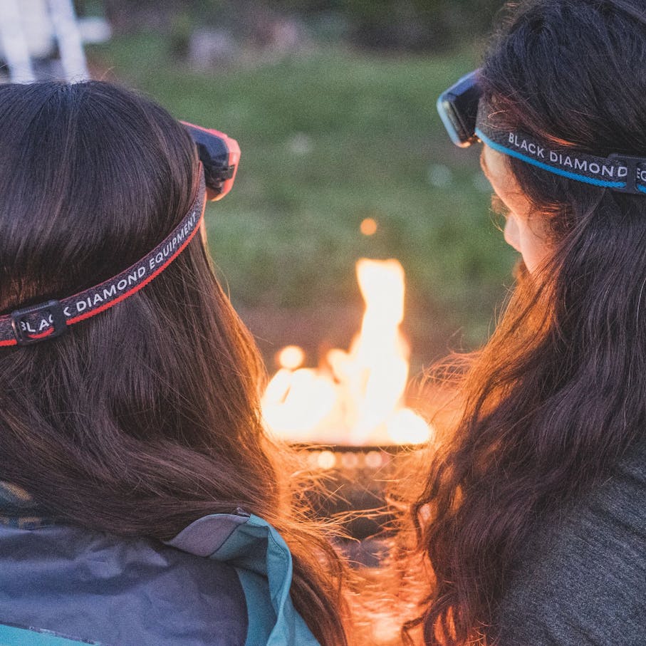 Two women wearing BD headlamps looking into a campfire