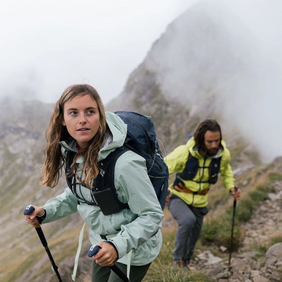 Two hikers in clouds in the Austrian alps hiking uphill with BD Apparel and Pursuit poles