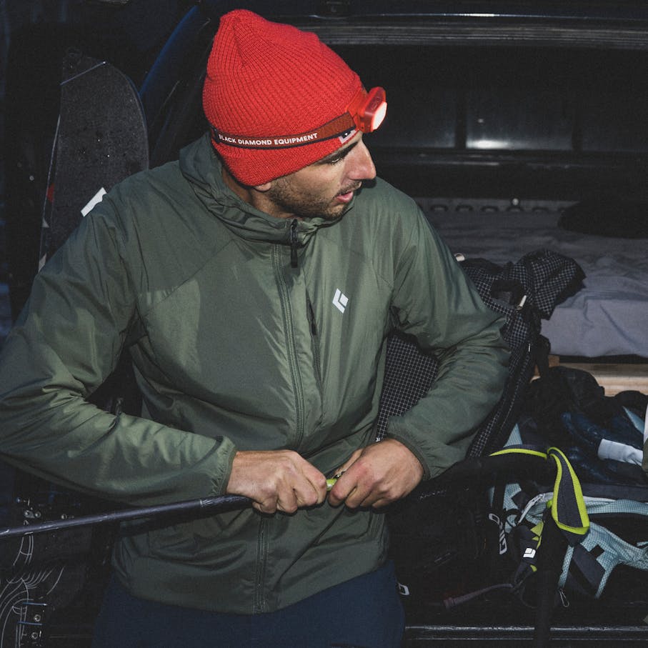 Un skieur de hors-piste portant le sweat à capuche isolé Alpine Start pour une Dawn Patrol.