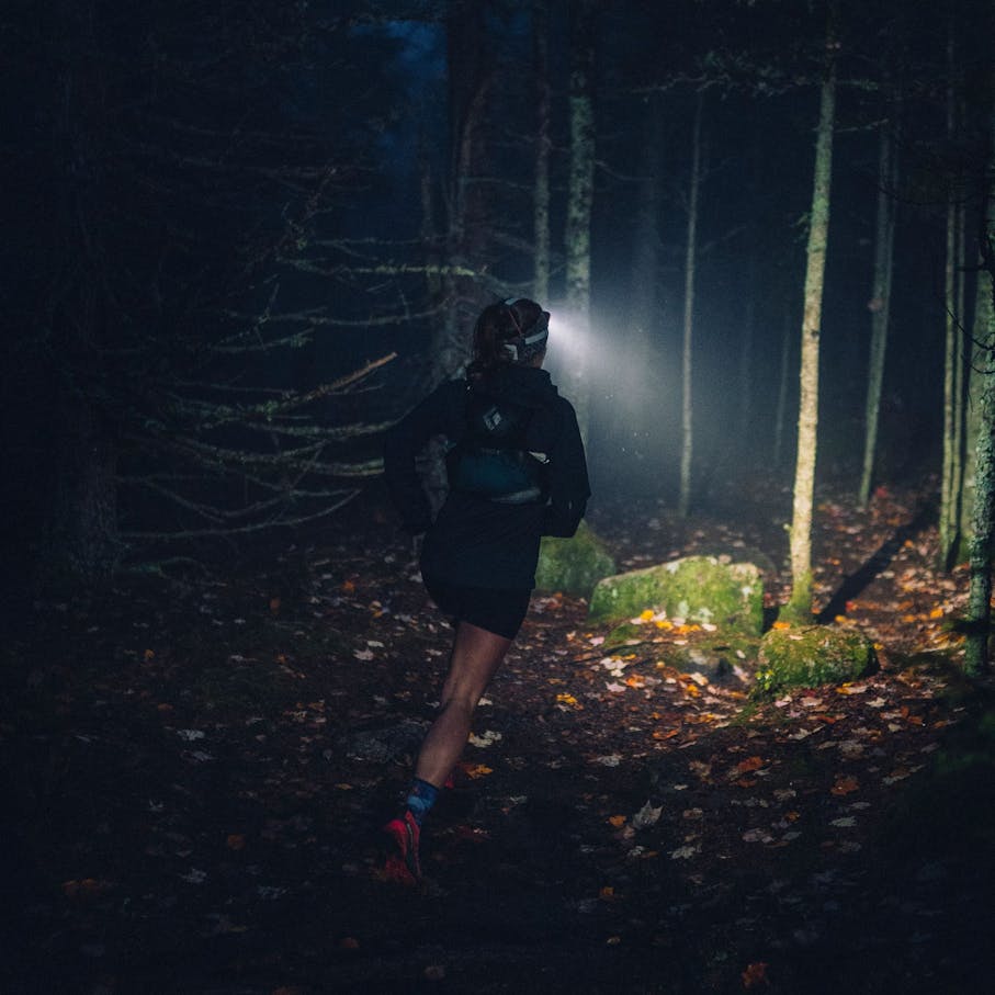BD Athlete Hillary Gerardi running in a dark forest with the Distance 1500 headlamp creating a beam