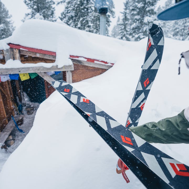 A splitboarder puts on her Black Diamond skins outside a yurt as the snow falls.