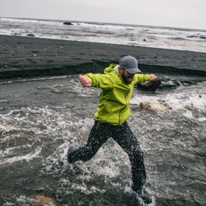 A hiker jumps in the surf on the ocean wearing Black Diamond rain gear. 