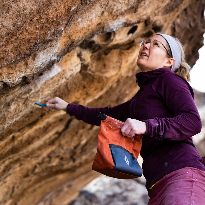 A boulderer brushes a hold while wearing a Black Diamond hoody.
