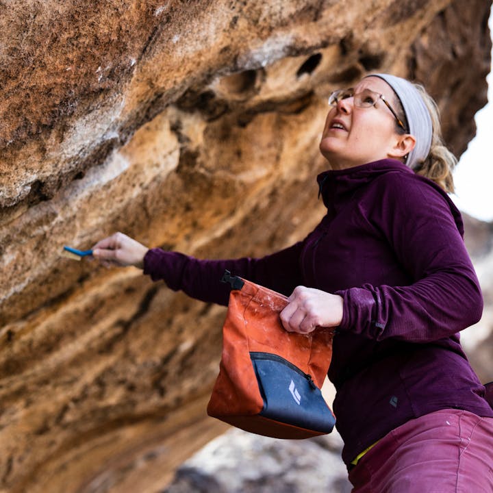 A boulderer brushes a hold while wearing a Black Diamond hoody.