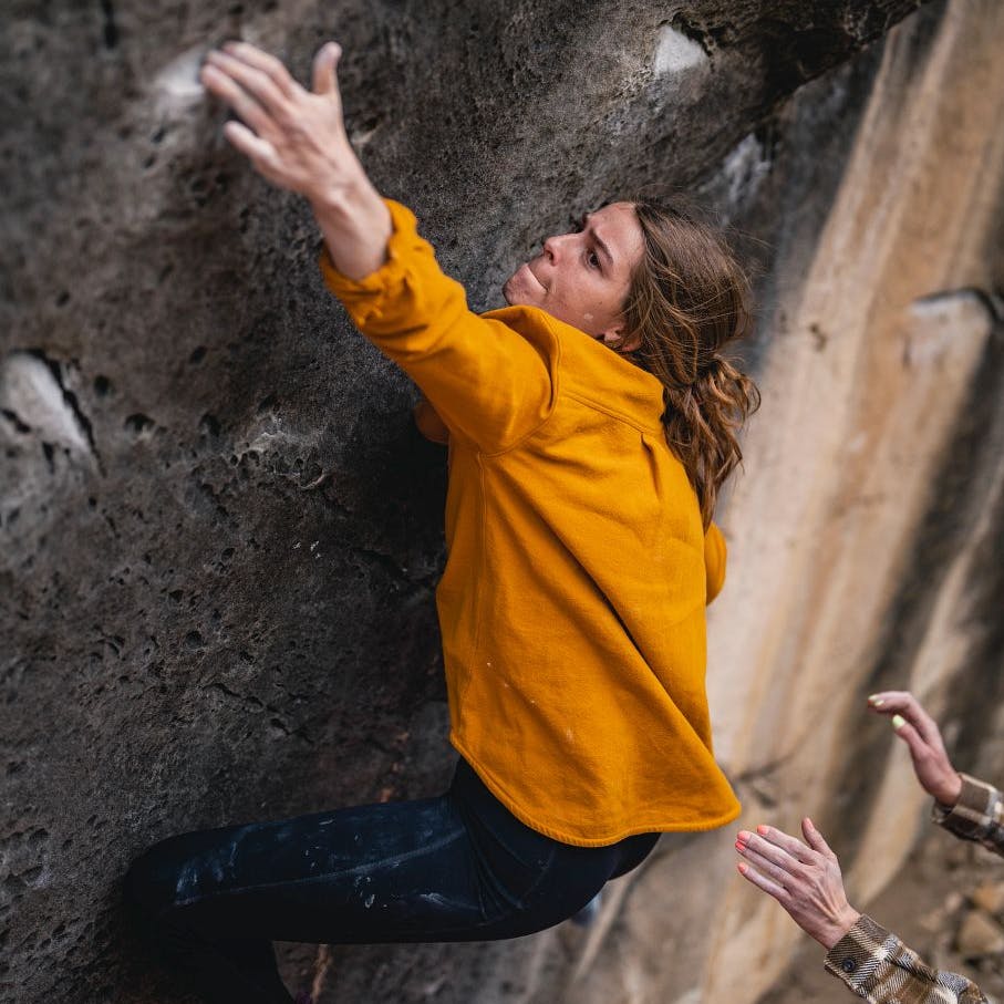 A boulderer reaches for a hold in the Women's Project Flannel.
