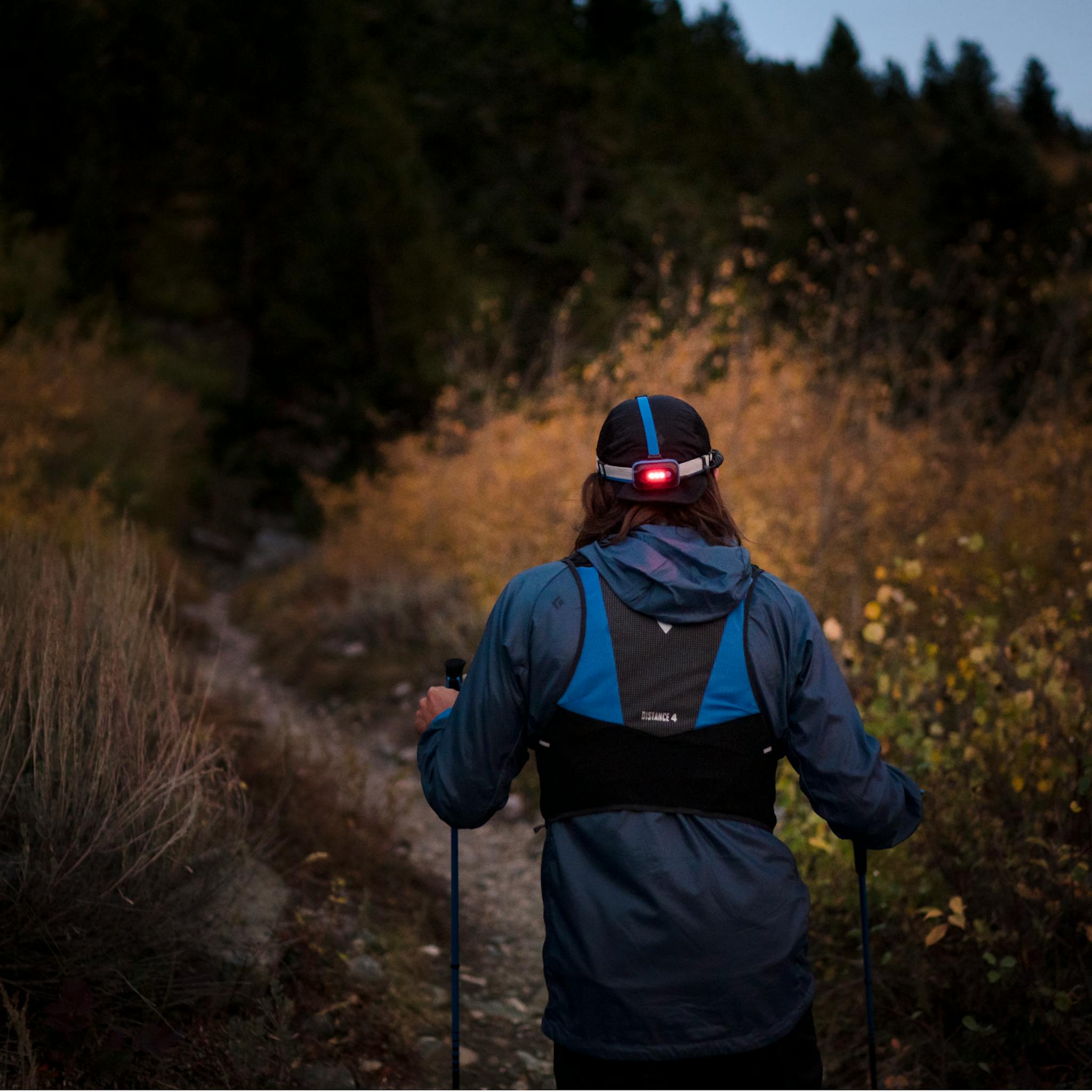 A hiker walks down a dimly lit trail, his Sprinter 500 Headlamp lighting the way.