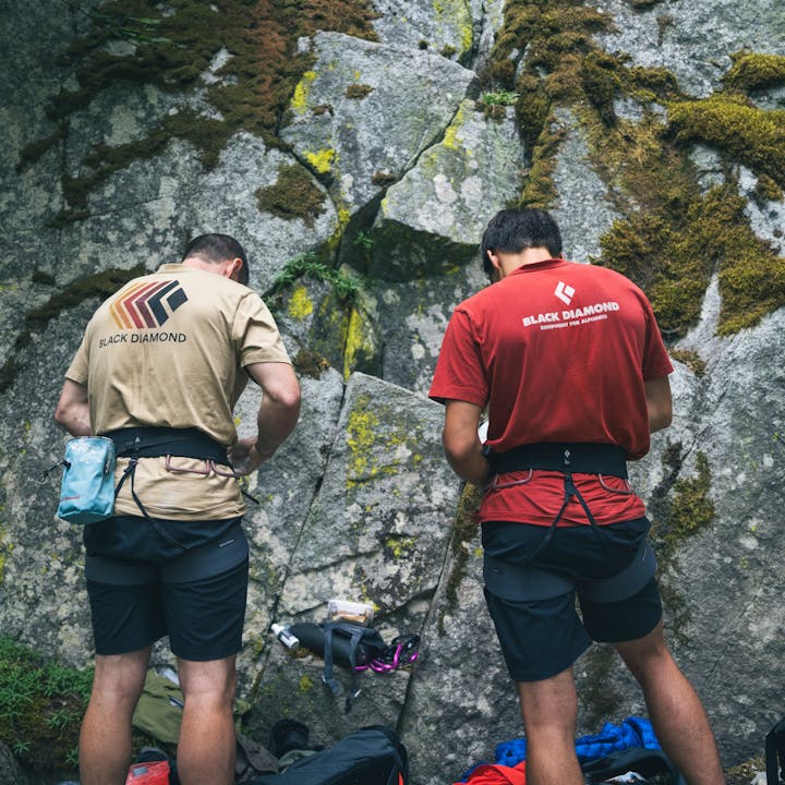 Two climbers rope up at the base of a cliff. 