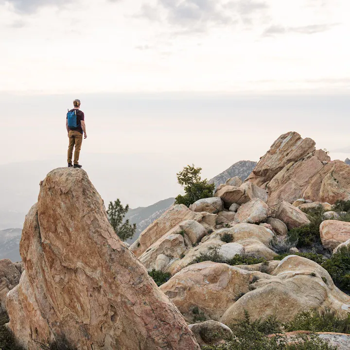 A photo by Christian Adam of a man standing on a boulder overlooking a vista.