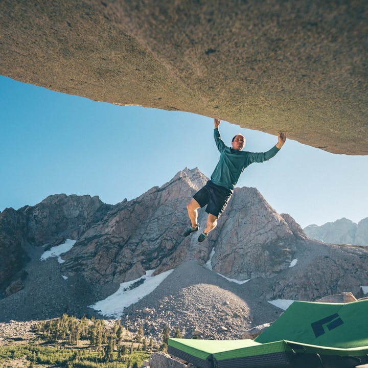 Carlo Traversi in an Alpenglow Hoody campuses on a boulder. 