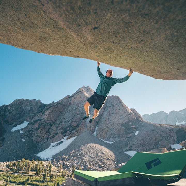 Carlo Traversi in an Alpenglow Hoody campuses on a boulder. 