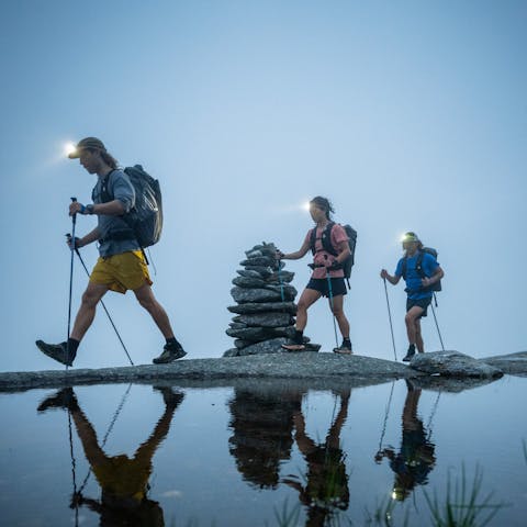 Three hikers in Beta Light Packs and BD headlamps walk by a cairn. 
