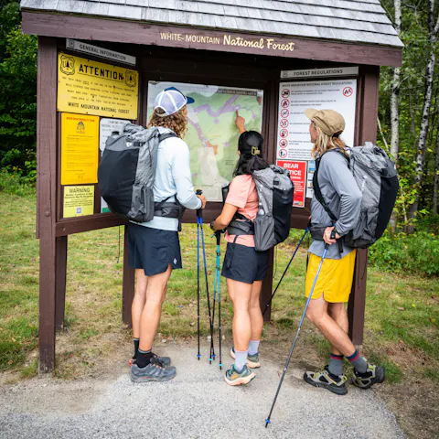 Three through hikers inspect a map while wearing Beta Light Series Backpacks. 