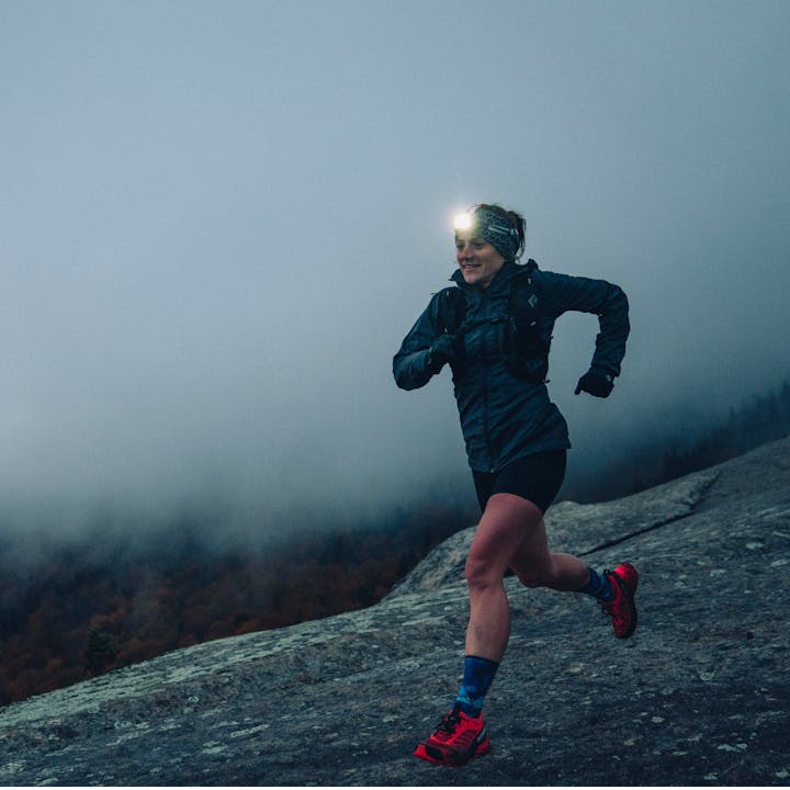In a Black Diamond headlamp, BD athlete Hillary Gerardi runs across a granite dome with cloudy skies behind. 