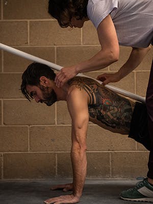 Photo of Esther Smith holding a pole on Sam Elias' back while he holds upper plank formation.