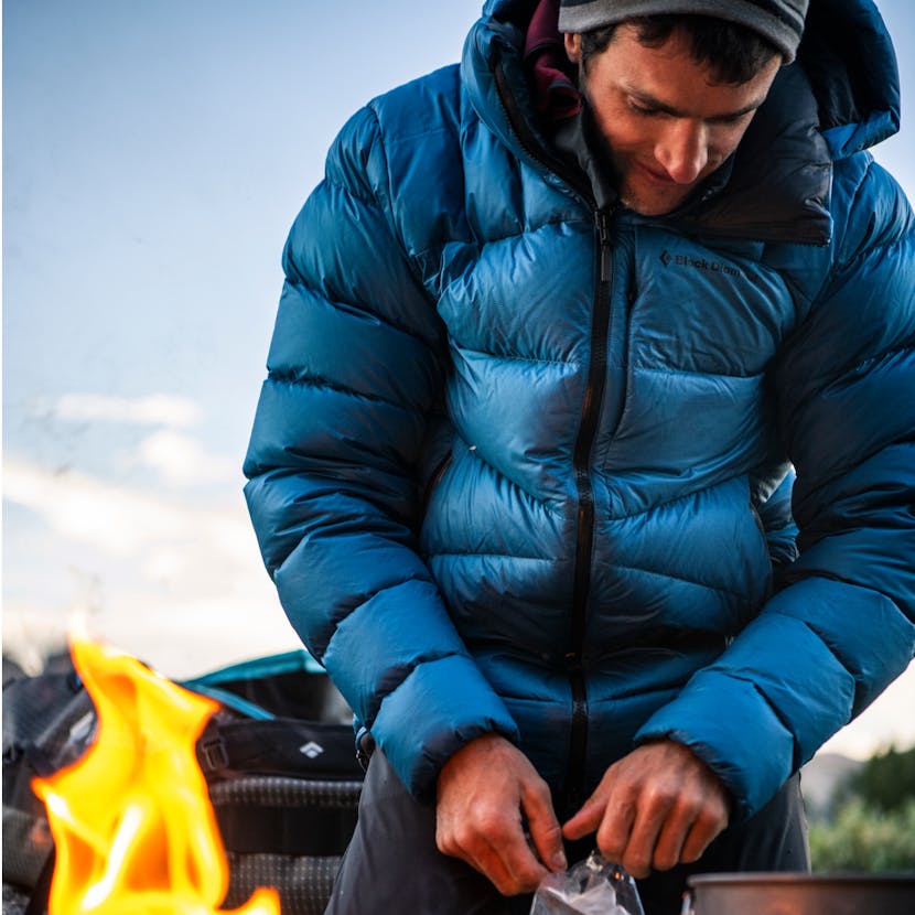Climber wearing the Black Diamond Vision Down Parka to stay warm while preparing breakfast at camp. 