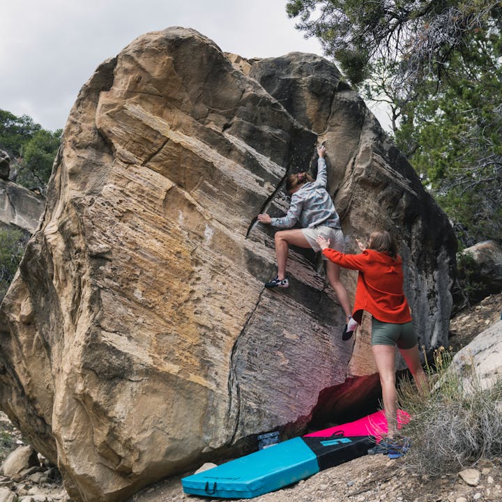 A boulderer readjusting her feet on the wall gets a spot from her friend in a Black Diamond Project Flannel. 