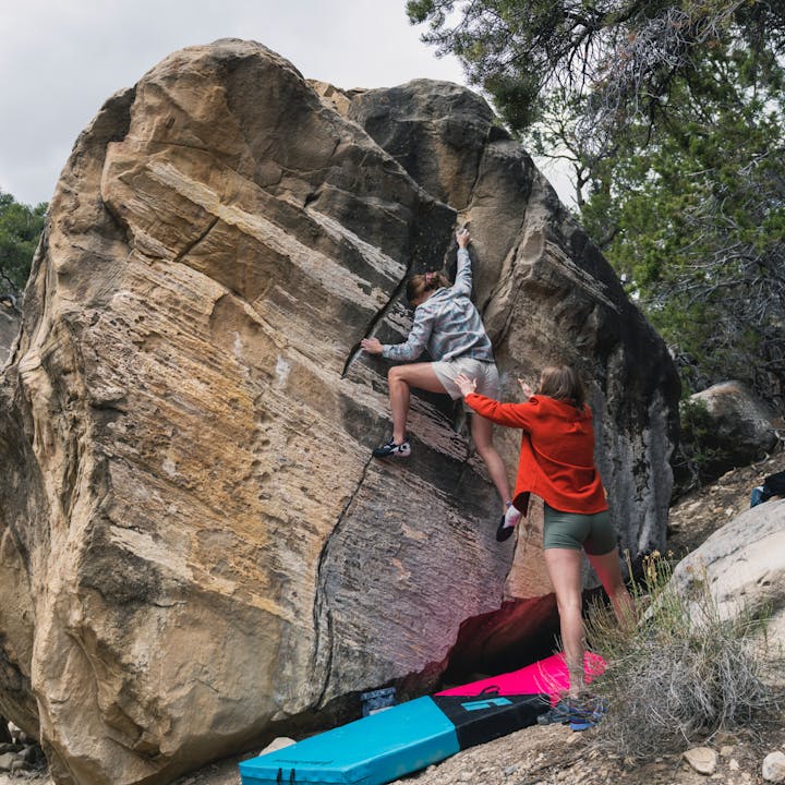 A boulderer readjusting her feet on the wall gets a spot from her friend in a Black Diamond Project Flannel. 