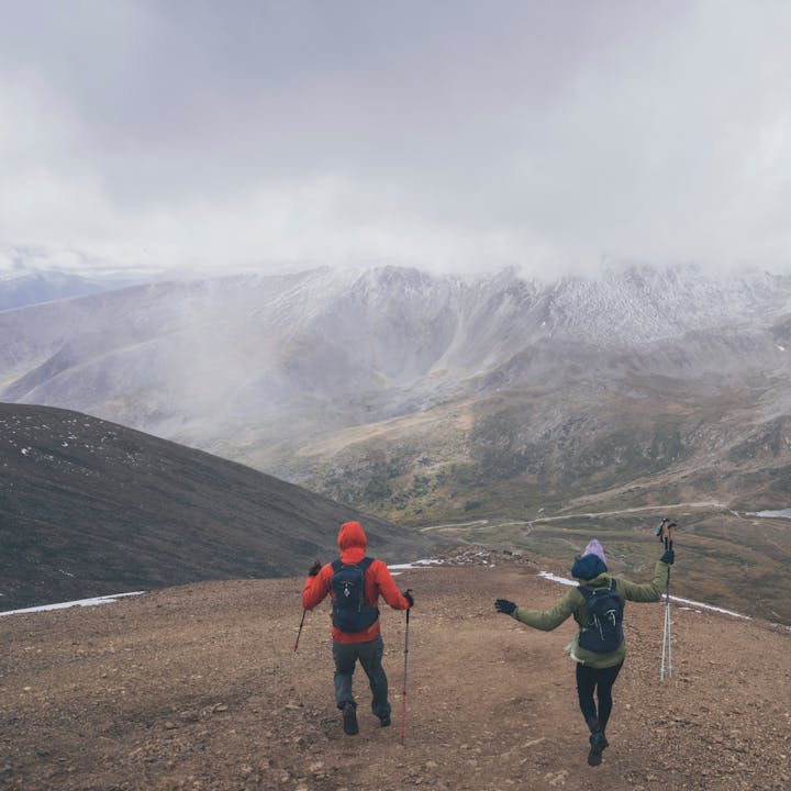 Two hikers run down mountain scree, their Black Diamond Pursuit Trekking Poles helping them down. 