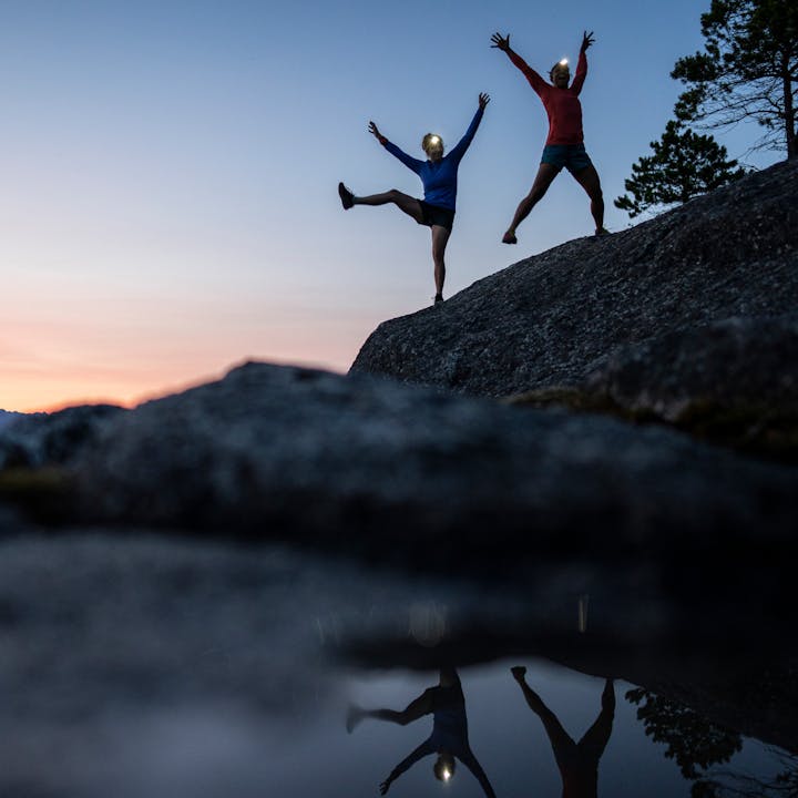 Two climbers jump for joy at twilight in BD headlamps.