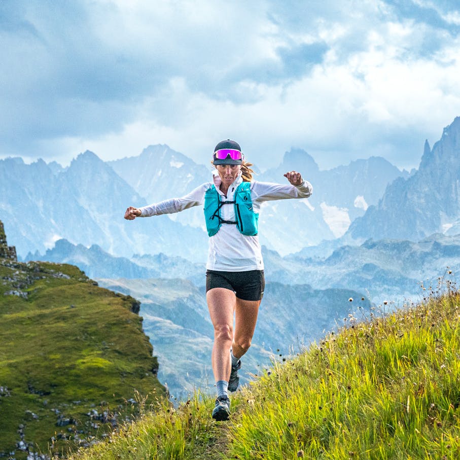 A runner on a grassy slope with looming mountains behind her.