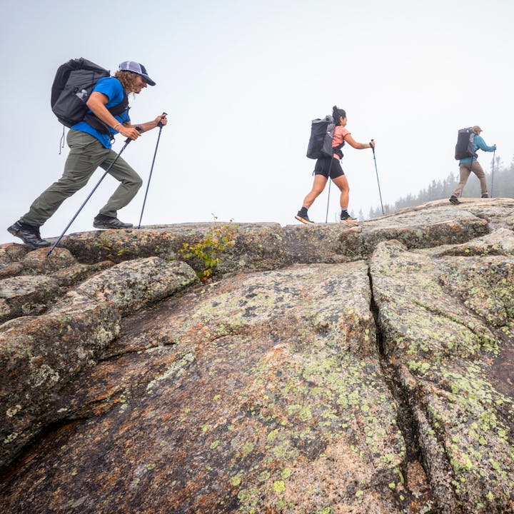 Three hikers in Betalight Packs trek across a granite dome. 