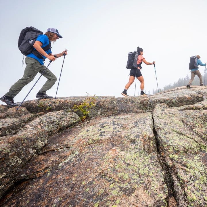 Three hikers in Betalight Packs trek across a granite dome. 