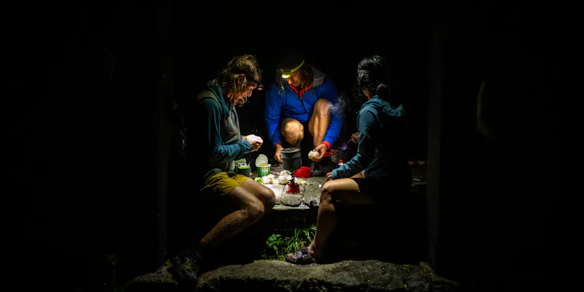 Some hikers cook dinner under headlamps at camp. 