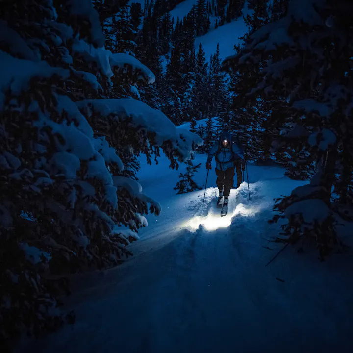 A backcountry skier uses their headlamp to light the way before the sun rises. 