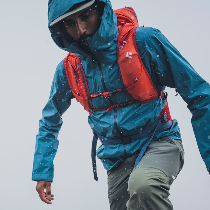 A hiker treks through rain in a Black Diamond Stormline Stretch Rain Shell. 
