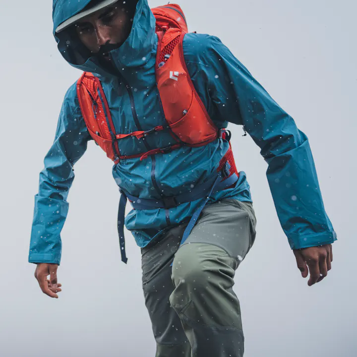 A hiker in the rain wears a Stormline Shell Rain Jacket. 