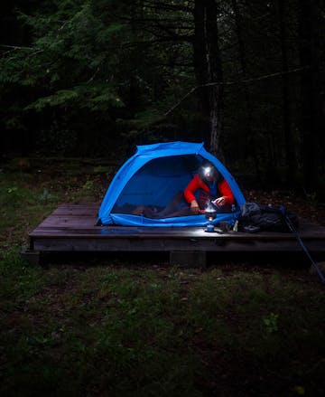 A through hiker cooks dinner in the Highline 2 person tent with their Black Diamond Headlamp. 
