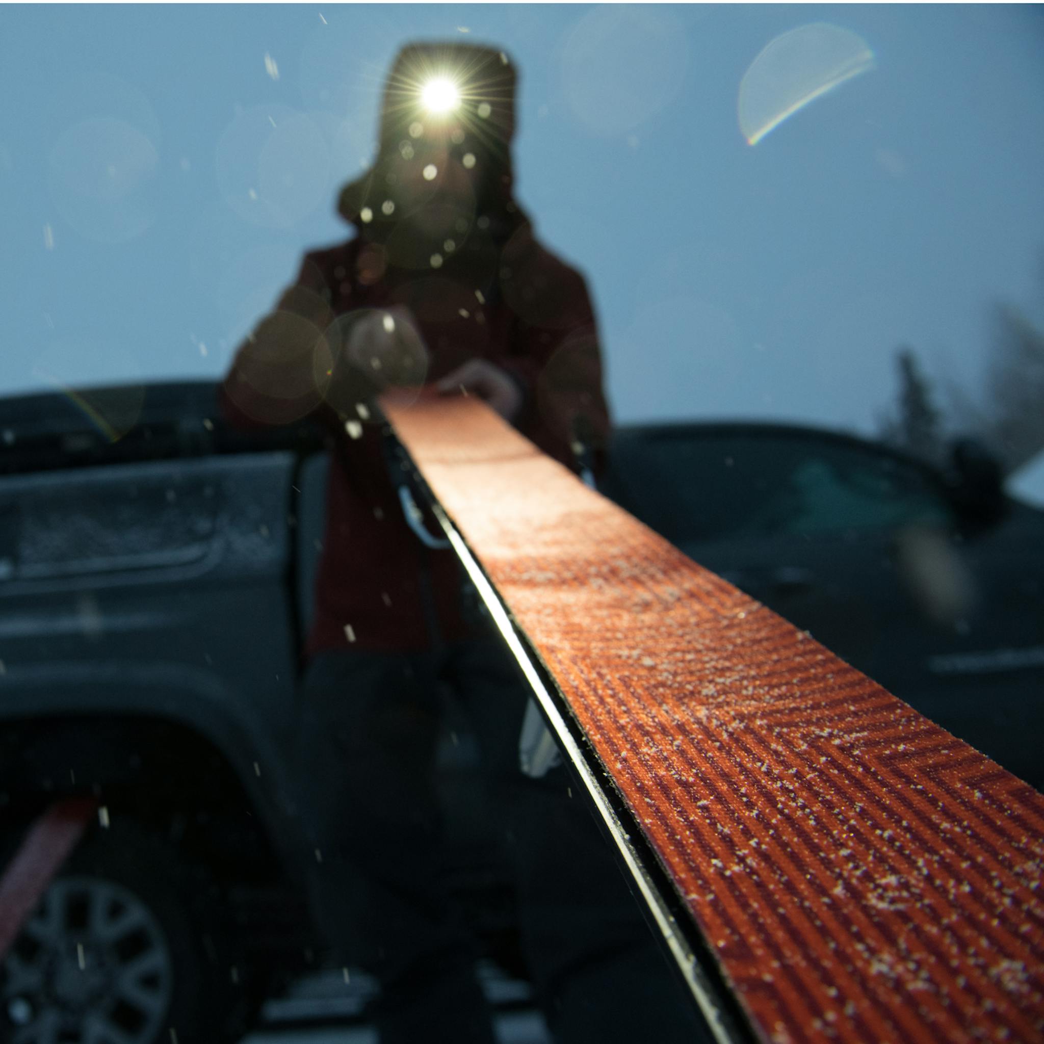 A skier with a BD headlamp puts skins on his skis.