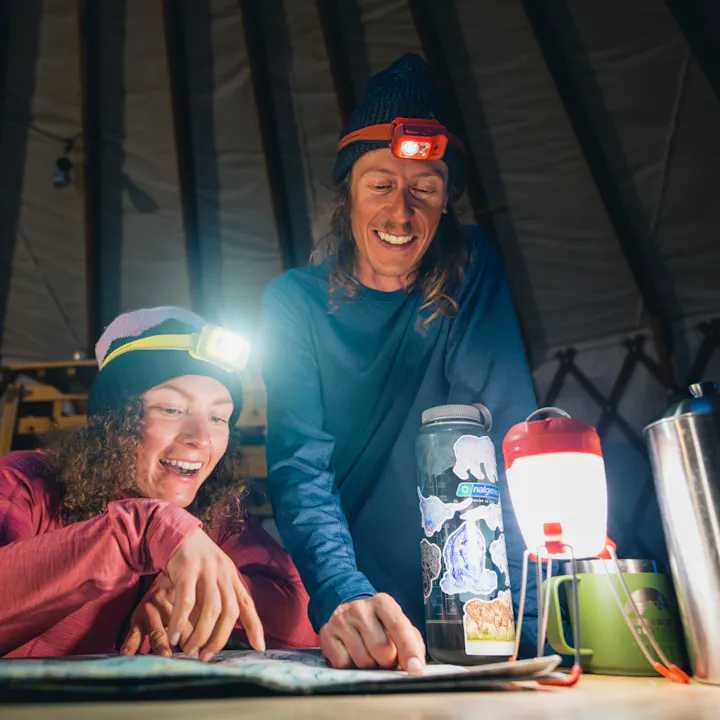 Two skiers plan tomorrow's tour in a cozy yurt lit by Black Diamond lanterns and headlamps. 