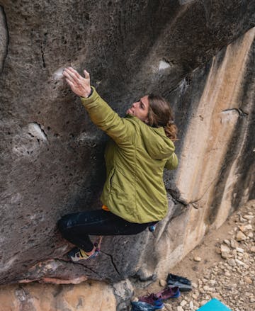 A climber wears the First Light Hoody to attempt a boulder problem and sticks a deadpoint. 